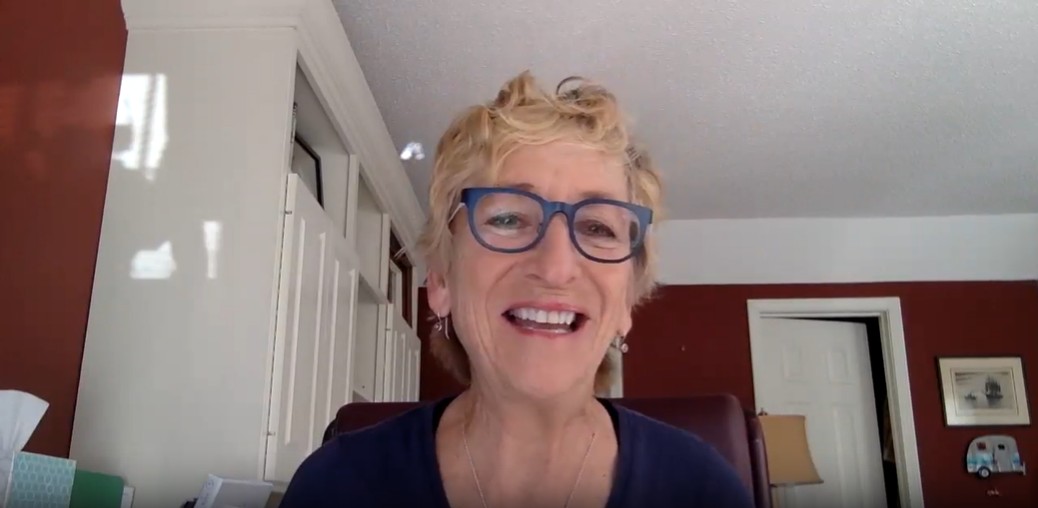 A picture of a short haired blonde woman  with glasses smiling on a Zoom call