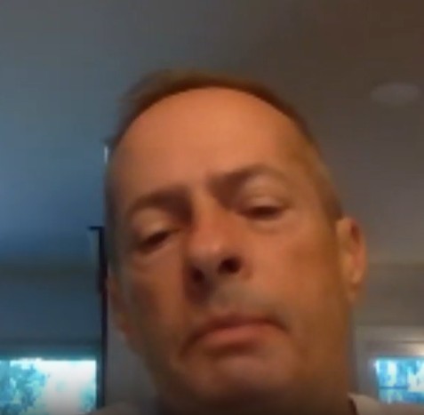 A picture of a man with grey hair looking down at his camera on Zoom